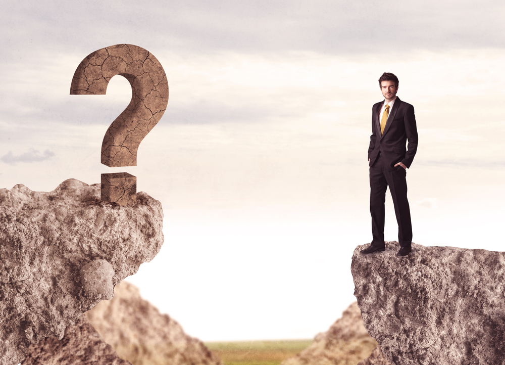 Businessman standing on the edge of mountain with a rock question mark on the other side