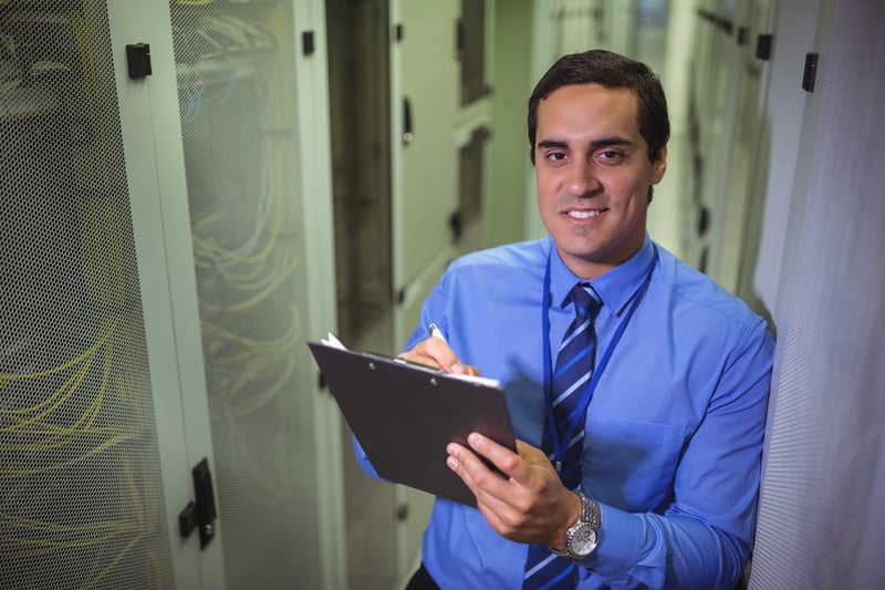 Technician maintaining record of rack mounted server on clipboard in server room